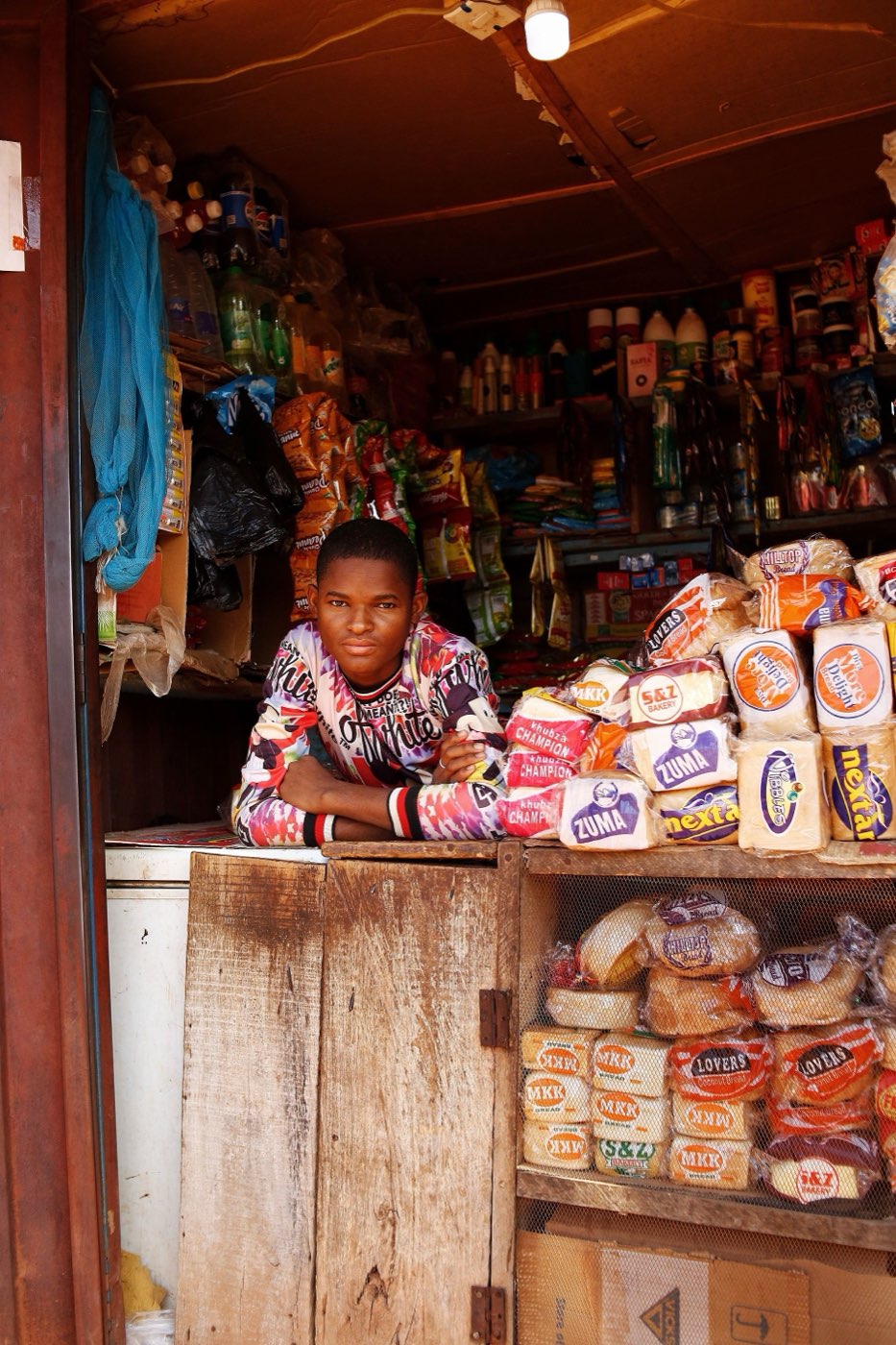 Commerçant dans sa boutique de quartier, entouré de ses marchandises